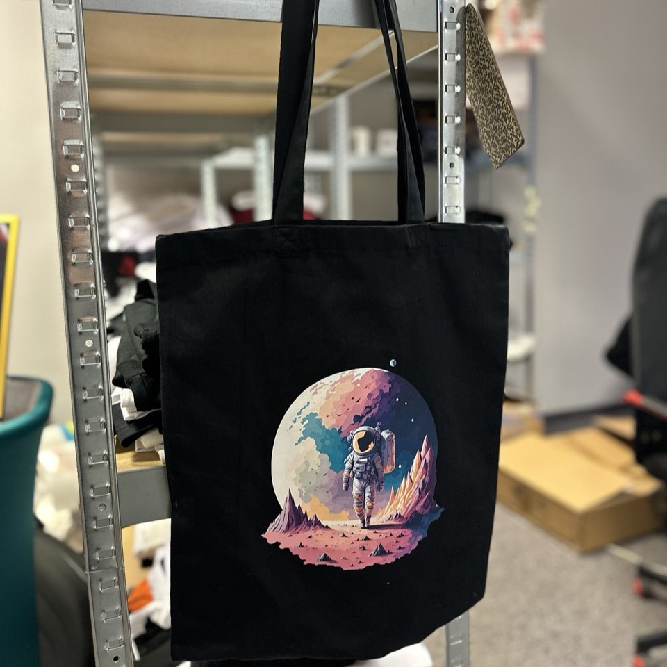 Black tote bag hanging in our office with a colourful astronaut and planet print – example of our work